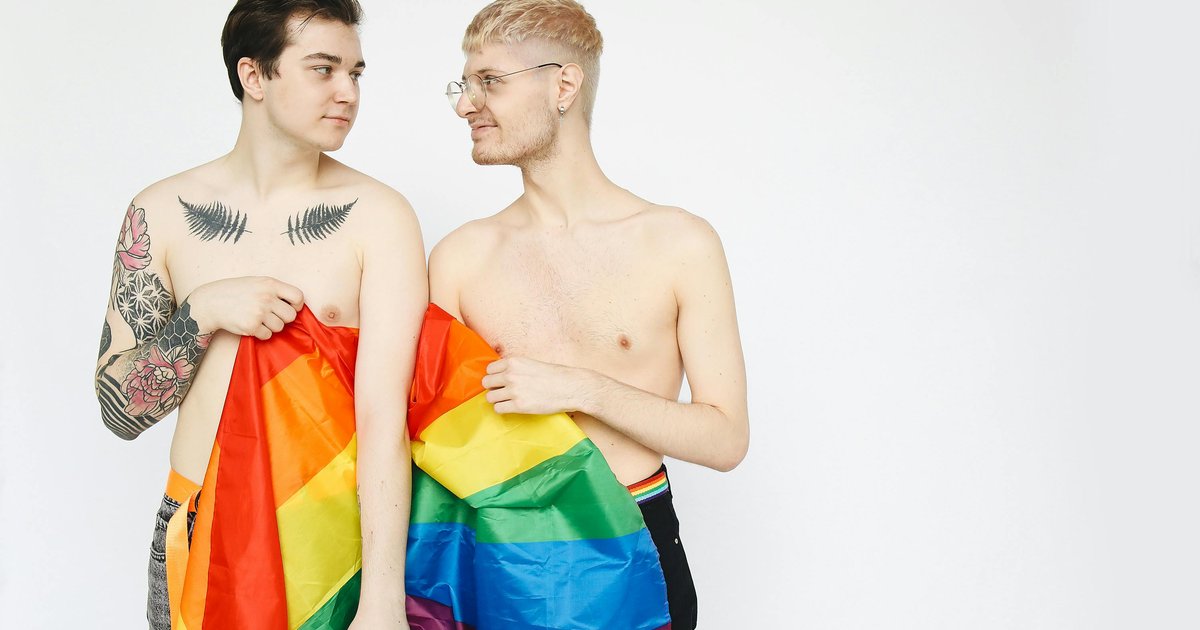 Jeune couple d'hommes gays drapé dans un drapeau arc-en-ciel LGBT, symbole de fierté et de coming out