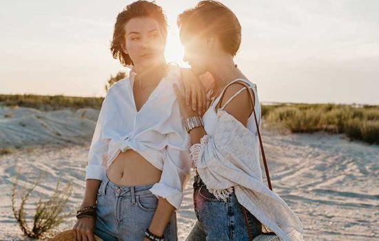Couple de femmes marchant main dans la main sur une plage au coucher du soleil, voyage lesbien